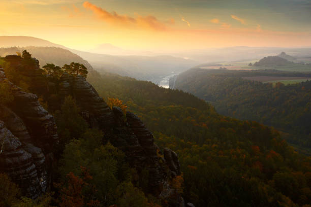 istock Schrammsteine, beautiful evening view over sandstone cliff into deep misty valley in Saxony Switzerland, foggy background, the fog is orange due to sunset, star sun on sky, Germany, with Elbe river 1253348473