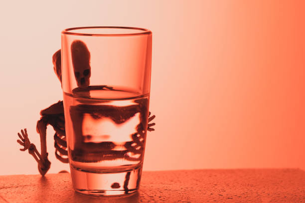 istock a skeleton peeps out from behind a glass of alcohol 1253349133