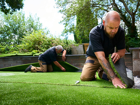 two workers fitting artificial grass in home garden