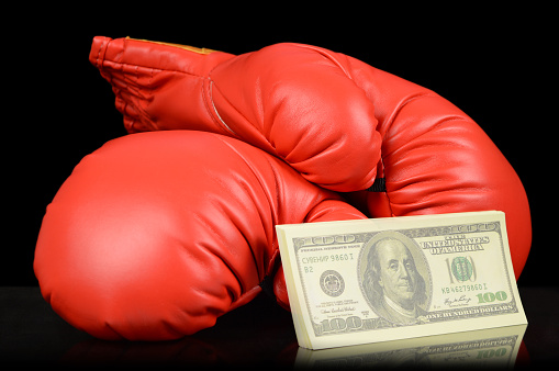 A pair of red boxing gloves with a stack of cash to place a gambling bet.