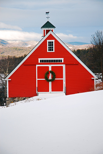 A red barn is decorated with a Christmas wreath in the highlands of New England