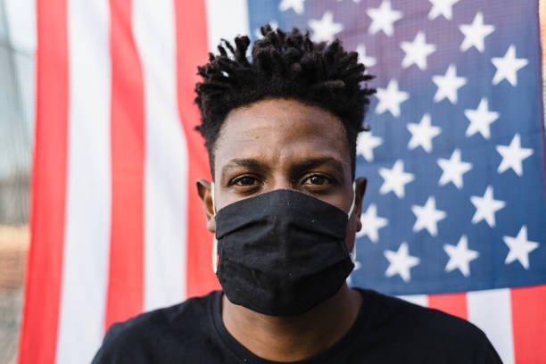 Covid-19: Man wearing protective mask with USA flag in the background Covid-19: Portrait of an American man wearing a face mask protestor photos stock pictures, royalty-free photos & images