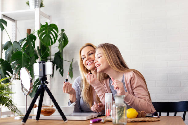 istock Mother and her daughter puting liquid lipstick on lips and record video about cosmetics on mobile phone 1253354661