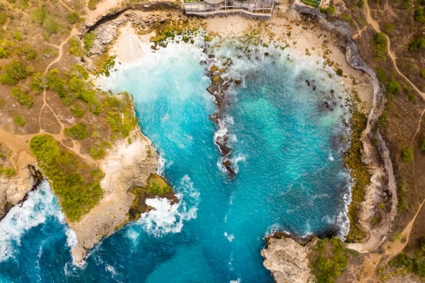 istock Top down aerial view of waves breaking inside a small rocky bay (Blue Lagoon, Nusa Ceningan, Indonesia) 1253359712