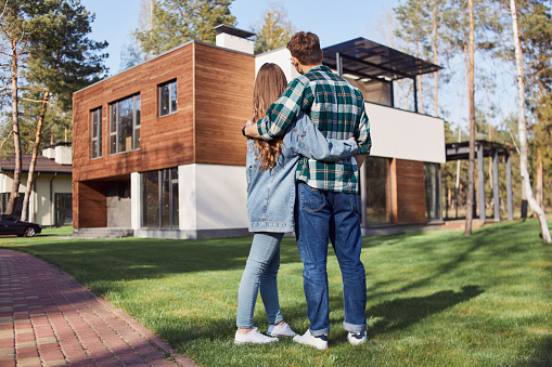 Full length of loving couple looking at their new house and hugging outdoors