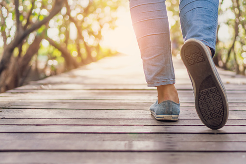 Woman is walking on small wood bridge to nature walk way with sunlight flare background.