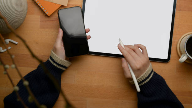 istock Female freelancer left hand holding smartphone and right hand working with mock-up tablet 1253379601
