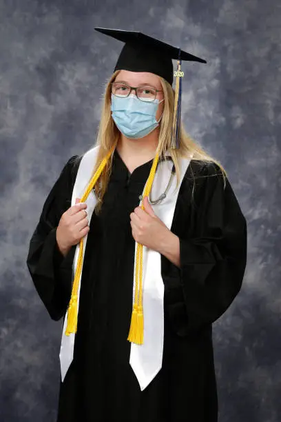 nurse graduated with BSN during COVID-19 pandemic. Shot in the studio with cap and gown, 2020 tassel, sash, and honors cord