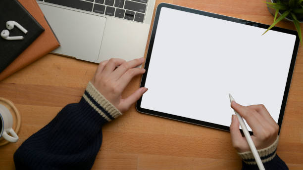 istock Female hands drawing on mock-up digital tablet on wooden worktable with laptop and schedule books 1253379656