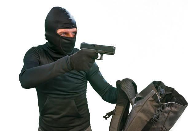 heist and robbery - Hollywood style portrait of man in balaclava mask holding gun in front of security metal vault door in bank or casino heist concept stealing money unlocking safe heist and robbery - Hollywood style portrait of man in balaclava mask holding gun in front of security metal vault door in bank or casino heist concept stealing money unlocking safe gun laws stock pictures, royalty-free photos & images