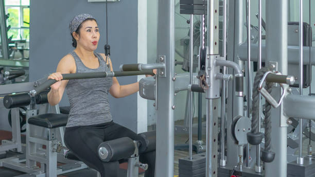 istock Fit woman using weight machine for arms workout at gym 1253384855