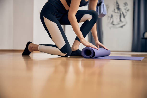 istock Slim woman rolling up yoga mat after session 1253384900
