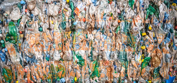 Close-up of compressed paper and plastic gathered into bundles and stacked outdoors at waste management facility.