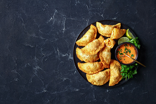 delicious deep fried Buffalo Chicken Empanadas with Low Calorie Dip on a black platter on a concrete table, horizontal view from above, flat lay, free space