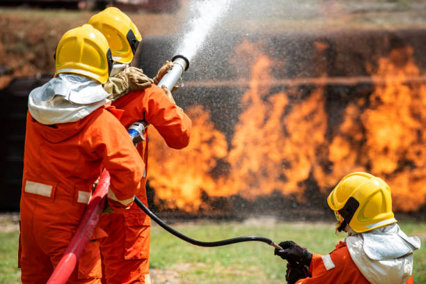 istock Group of firefighter in fire suit using water and chemical foam from fire Extinguisher Hose fight with fire flames inside burning premises. Fireman teamwork spraying high pressure water fight a fire. 1253392108