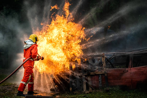 istock Brave firefighter in fire suit on rescue duty using water from hose extinguishing fighting with big crackle fire flames inside burning premises. Fireman spraying high pressure water fight a fire 1253392117