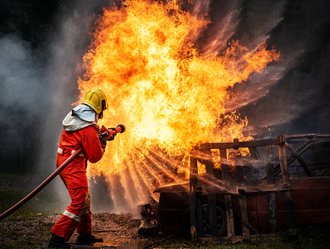 Valiente bombero en traje de fuego en servicio de rescate utilizando agua de la extinción de mangueras luchando con grandes llamas de fuego crepitante dentro de las instalaciones en llamas. Bombero rociando agua de alta presión lucha contra un incendio photo