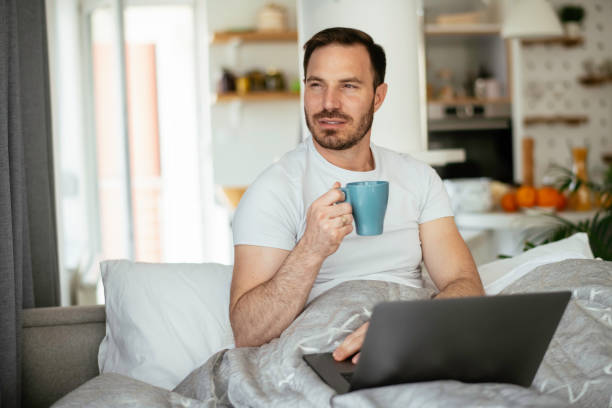 istock Young man watching a movie in bed and drinking coffee. 1253394058