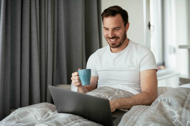 istock Young man watching a movie in bed and drinking coffee. 1253394071