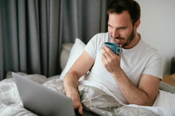 istock Young man watching a movie in bed and drinking coffee. 1253394102
