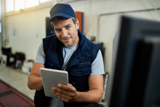 istock Smiling mechanic using digital tablet in auto repair shop. 1253396402