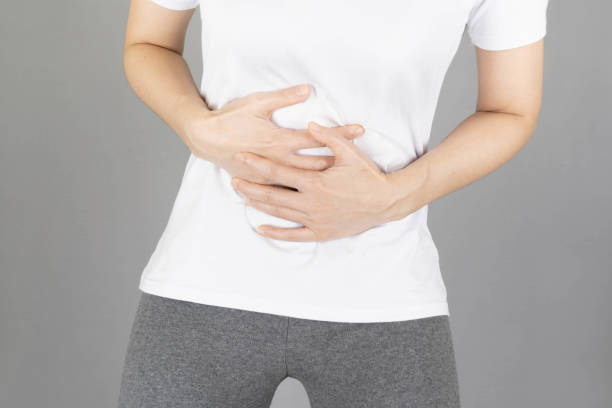 A human having painful stomachache on gray background.Chronic gastritis. Abdomen bloating concept.Close-up Of Woman using hands touching belly position suffering during menstruation period un humano que tiene dolor de estómago doloroso en el fondo gris. gastritis crónica. concepto de hinchazón del abdomen. primer plano de la mujer usando las manos que tocan la posición del vientre sufriendo durante el período de la menstruación