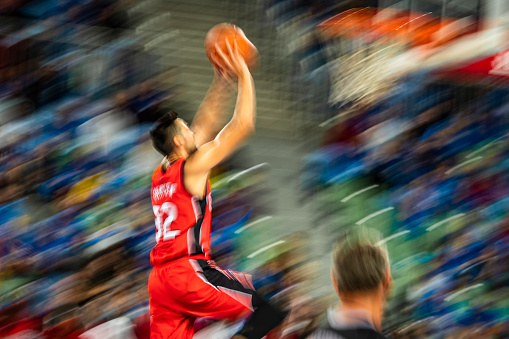 Blurred motion of basketball player aiming ball for hoop during the match in stadium.