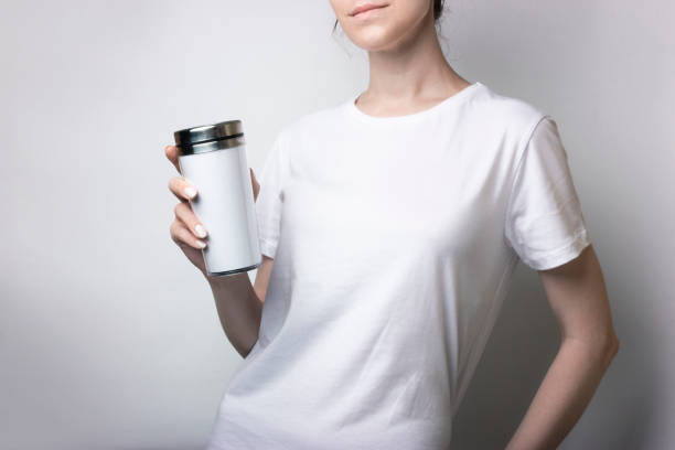 흰색 티셔츠를 입은 소녀가 커피와 함께 써모컵을 들고 있다. 브랜딩을 위한 공백. 흑백 모형 - insulated drink container 뉴스 사진 이미지