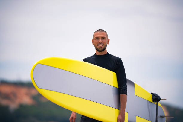 istock Young and fit surfer smiling and looking forward with yellow surfboard on a sunny summer day. Vacation outdoor activity. 1253405178