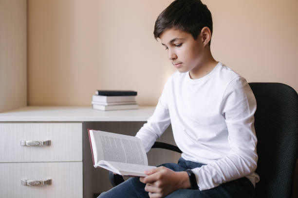 istock Young boy sitting by the desk and read the book. Study at home during quarantine 1253405214