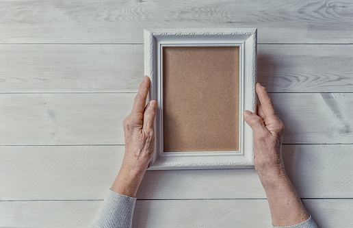 Elderly woman looking at the picture, light wodden background. Empty template, mock-up. Happy memories, sadness, nostalgia concept.