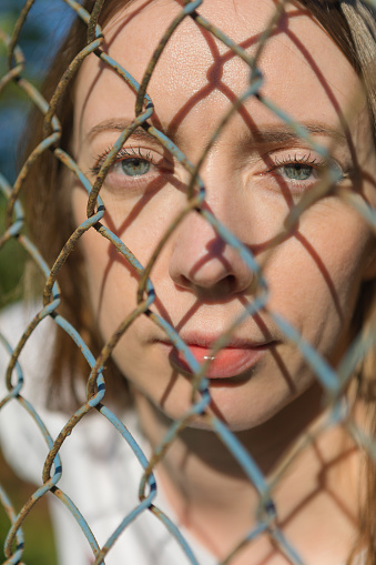 Close-up face of a young girl looking through a metal fence.