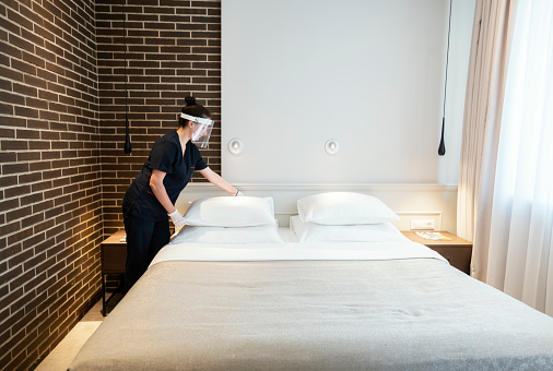 Maid doing the bed wearing a face mask while working at a hotel during Covid-19