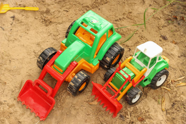 Sherwood, Oregon, USA - August 27, 2015: Row of yellow TONKA toy dump trucks in a sand play area in a city park is the main focus across the image. The trucks have sand in them put in from kids digging in the sand. Toy shovels and other play items are also visible in this large sand box. 