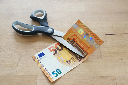 Euro banknote is cut with scissors, business concept for German lower MwSt (value added tax), wage reduction and pay less money during coronavirus pandemic, wooden table, copy space