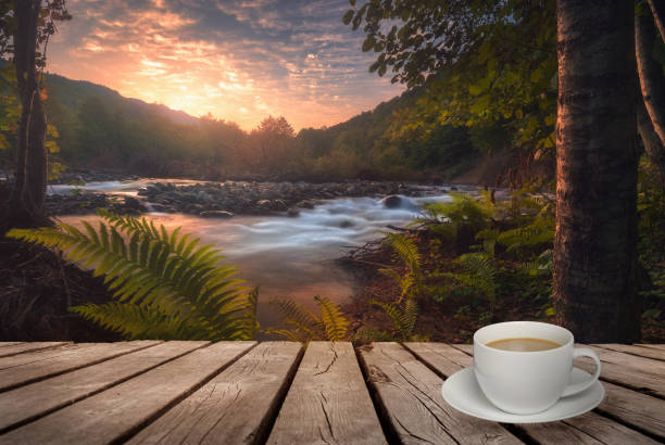 Close up white coffee cup on wood table and view of beautiful sunrise river background. Natural template landscape