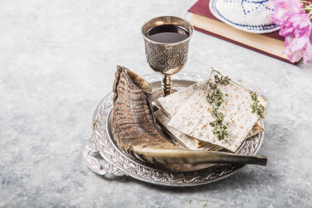 istock Metal plate with matzah or matza, Kiddush Cup, Shofar horn  on a light  background presented as a Passover seder feast or meal with copy space. Jewish traditional objects, yarmulke, Tallit, Prayer book 1253424159