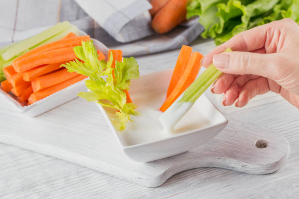 Vegetable sticks. Fresh celery and carrot with yogurt sauce. Healthy and diet food concept Vegetable sticks. Fresh celery and carrot with yogurt sauce. Woman's Hand holding celery stick. Healthy and diet food concept. dip stock pictures, royalty-free photos & images