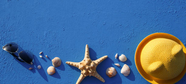 istock Frame with beach accessories on a nautical theme: yellow straw hat, sunglasses, starfish and shells on a blue background. 1253426280