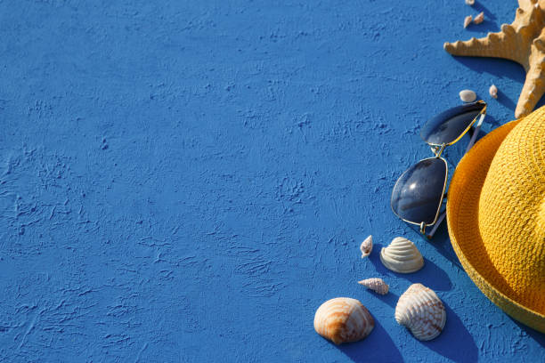 istock Frame with beach accessories on a nautical theme: yellow straw hat, sunglasses, starfish and shells on a blue background. 1253426287