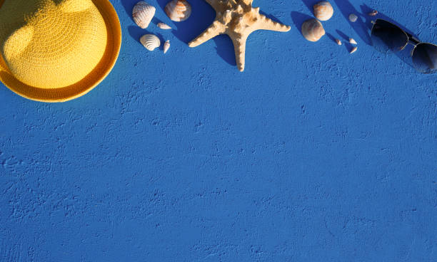 istock Frame with beach accessories on a nautical theme: yellow straw hat, sunglasses, starfish and shells on a blue background. 1253426290