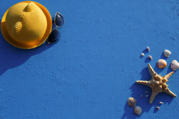 istock Frame with beach accessories on a nautical theme: yellow straw hat, sunglasses, starfish and shells on a blue background. 1253426307