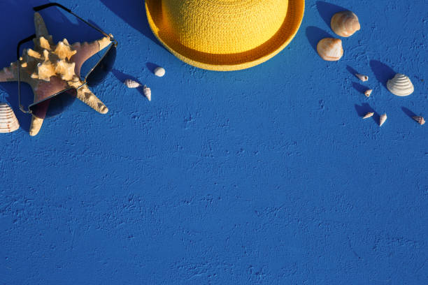 istock Frame with beach accessories on a nautical theme: yellow straw hat, sunglasses, starfish and shells on a blue background. 1253426311