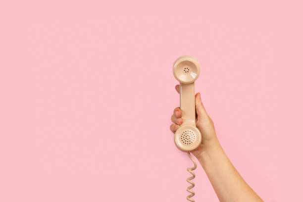 Woman´s hand holding an old phone on a pink background Woman´s hand holding an old phone on a pink background with copy space telephone receiver stock pictures, royalty-free photos & images