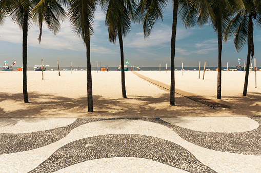 Iconic black and white sidewalk tile pattern and palm trees at Copacabana Beach in Rio de Janeiro, Brazil.
