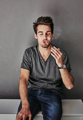 Cropped shot of a beaten and bruised young man smoking a cigarette
