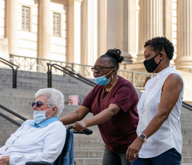 two caretakers, elderly woman in wheelchair, masks pass the metropolitan museum of art during coronavirus - group of people art museum clothing lifestyles imagens e fotografias de stock