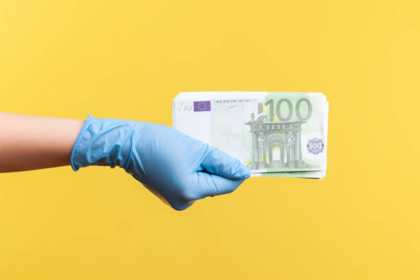 profile side view closeup of human hand in blue surgical gloves holding and showing fan of european union euro money in hand - european union coin european union currency coin isolated objects imagens e fotografias de stock