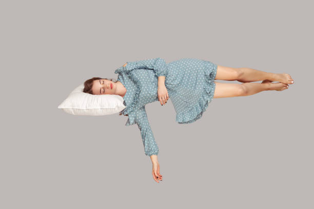 空中でホバリング眠れる美女。ヴィンテージフリルドレスを着たリラックスした女の子が枕浮上に快適に横たわっている - adult sleeping women one person ストックフォトと画像