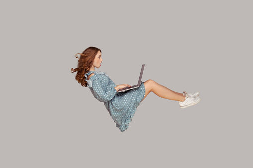 Hovering in air. Surprised girl ruffle dress levitating, looking at laptop screen shocked amazed, surfing web social networks